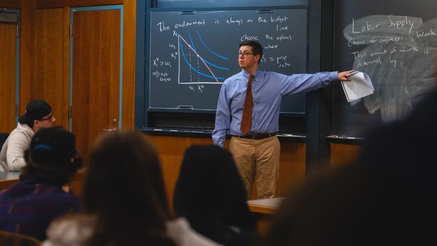 Assistant Professor of Economics Ben Chartock stands in front of a chalkboard in a classroom while teaching Bentley students.