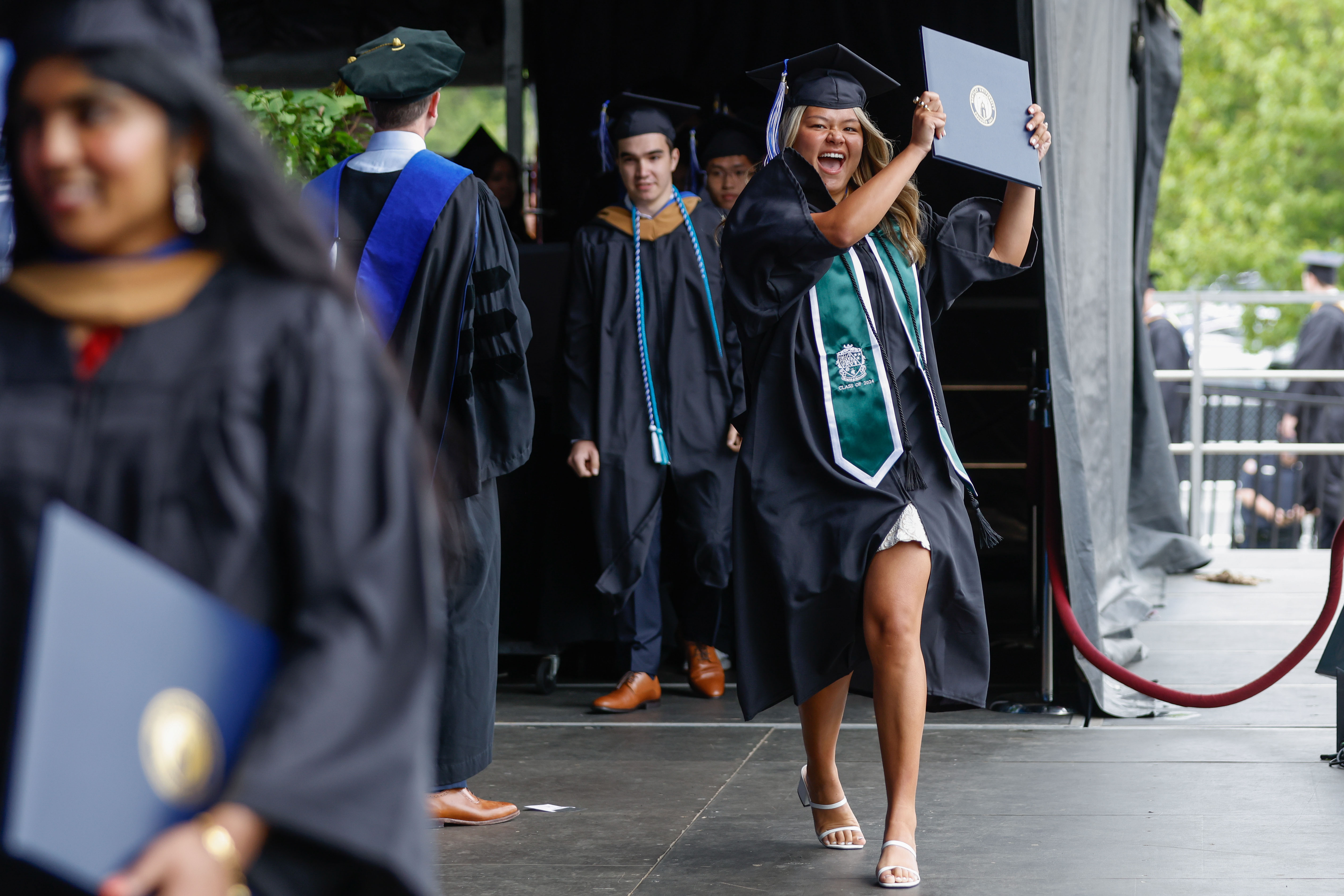 A student holds up her diploma triumphantly as she crosses the stage