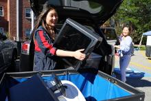 Student wearing navy blue jacket with red stripe unpacking bin from car