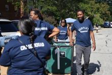 Members of Bentley basketball team wearing blue t-shirts pushing green rolling bin