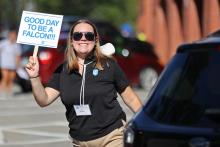 Bentley orientation leader wearing black shirt and holding a sign that says "Good day to be a Falcon"