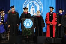 Bentley faculty and staff wearing regalia on stage standing around podium for Convocation