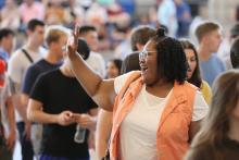 Student wearing white shirt and orange vest waving at family