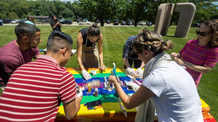 a group of people gathered around a table making tie dye canvas bags